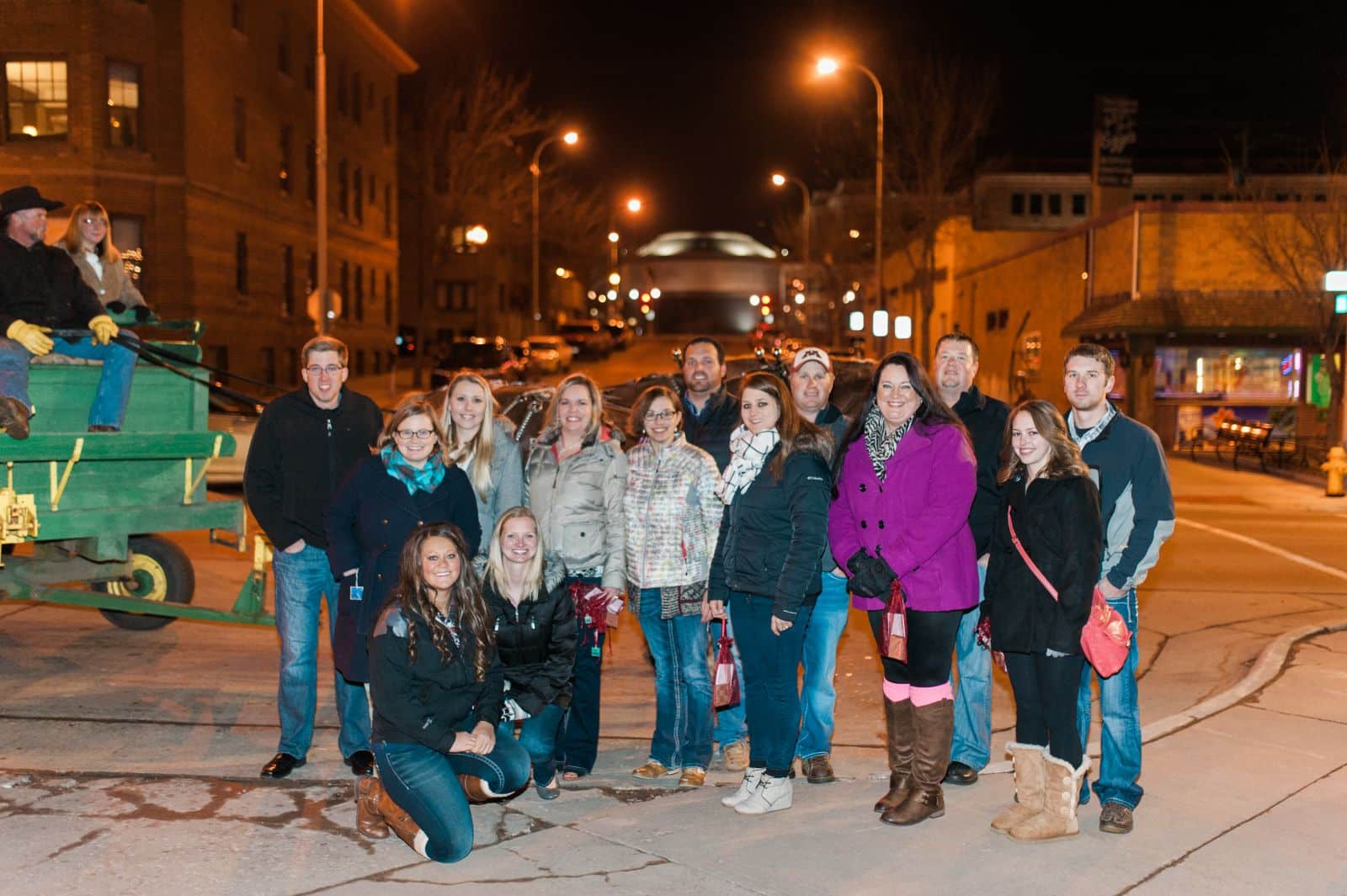 Large group of people posing together on a nighttime street, smiling at camera for team photo.