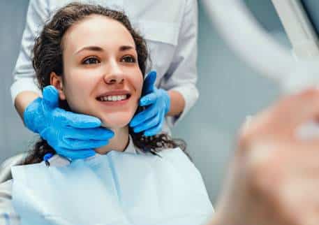 Woman smiling during dental examination with dentist wearing blue gloves in clinical setting.