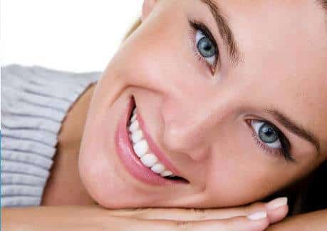 Woman smiling at camera, resting head on hand, showcasing bright teeth and cosmetic dentistry results.