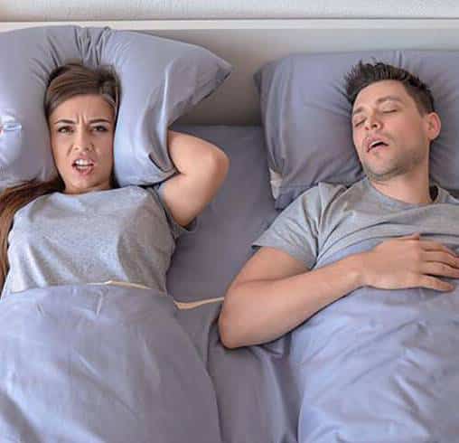 Two people lying in bed looking unwell or tired, illustrating sleep or dental health concerns.