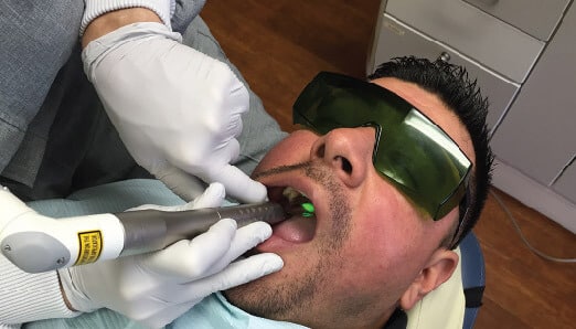 Dentist performing dental examination on male patient wearing protective eyewear in clinical setting.