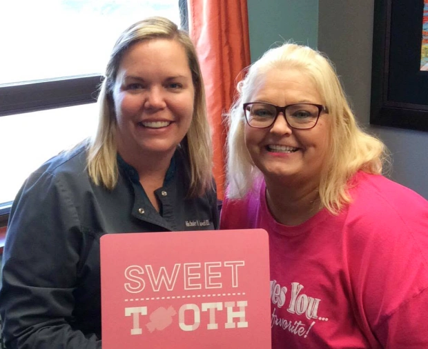 Two smiling women holding a pink “Sweet Tooth” sign