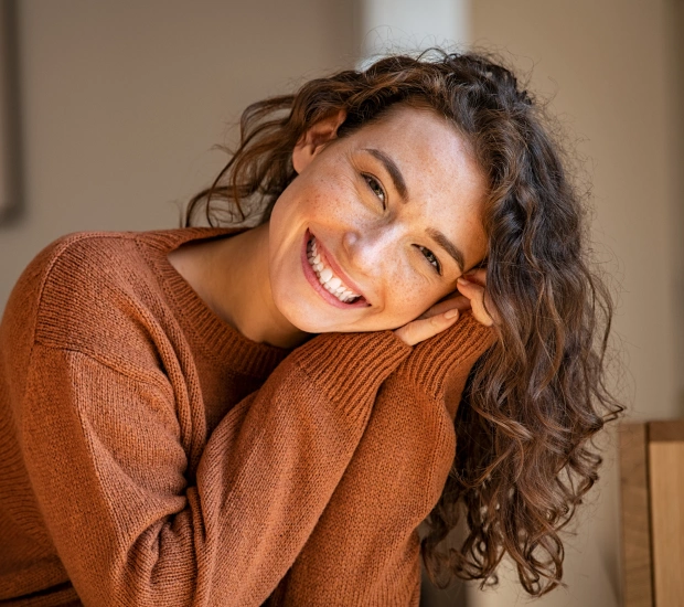 Smiling woman with curly hair wearing an orange sweater