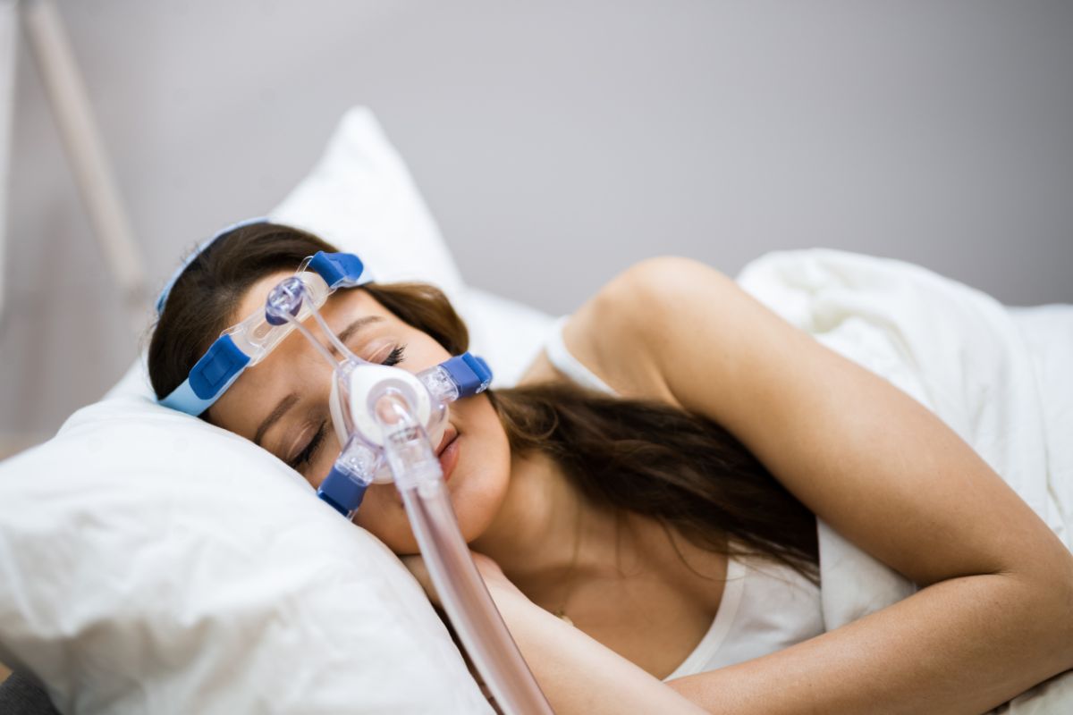 A woman sleeping on her side while wearing a CPAP mask connected to a breathing tube to help manage obstructive sleep apnea.